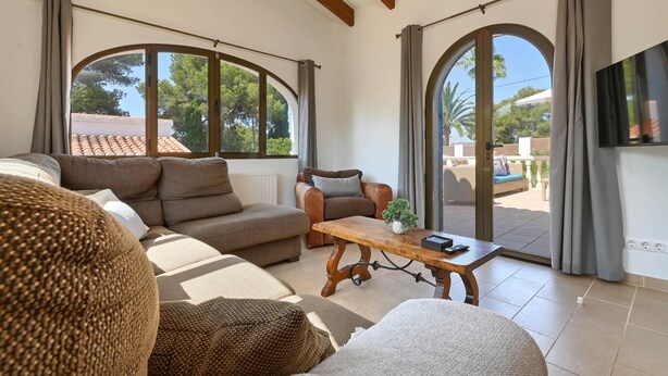 A spacious living room with a sofa, armchairs, and a coffee table. Large arched windows provide natural light and a view of the outdoors. - Casa Virginia 6 pax - Javea, Costa Blanca (Javea)