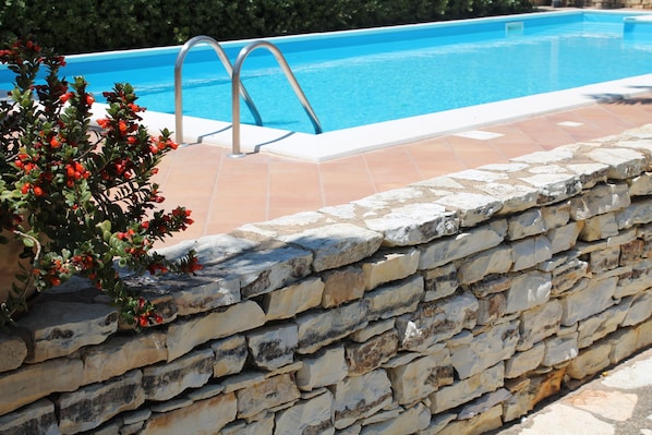 A stone wall with a pool and metal ladder.
