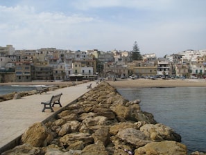 A coastal promenade with a rocky breakwater, benches, and a row of buildings in the background.