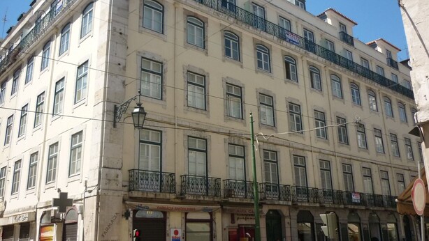 Un immeuble à plusieurs étages de style architectural classique, doté de balcons, de grandes fenêtres et d’une entrée au niveau du sol avec une enseigne indiquant la présence d’une pharmacie et d’autres commerces.