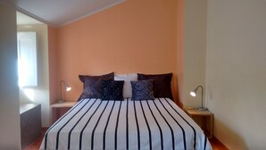 Une chambre à coucher avec une couvre-lit à rayures, deux lampes de chevet et une fenêtre avec des stores.