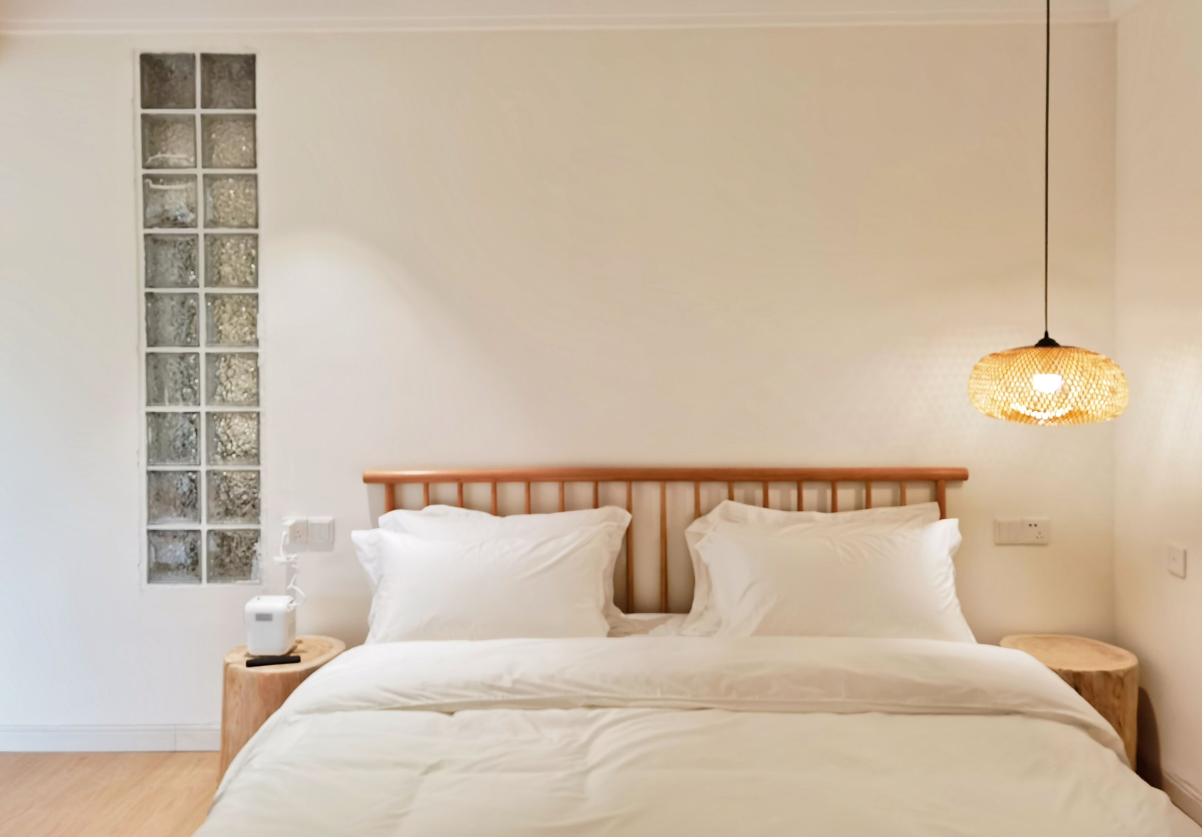 Un dormitorio con cabecera de madera, ropa de cama blanca, una mesita de noche con lámpara y una ventana con vistas.