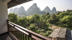 A traditional house with a tiled roof and a balcony overlooking a lush garden and distant mountains. - Riverside Retreat Hotel (Guilin)