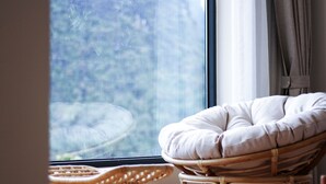 A wicker chair with a cushion near a window with a view of trees. - Riverside Retreat Hotel (Guilin)