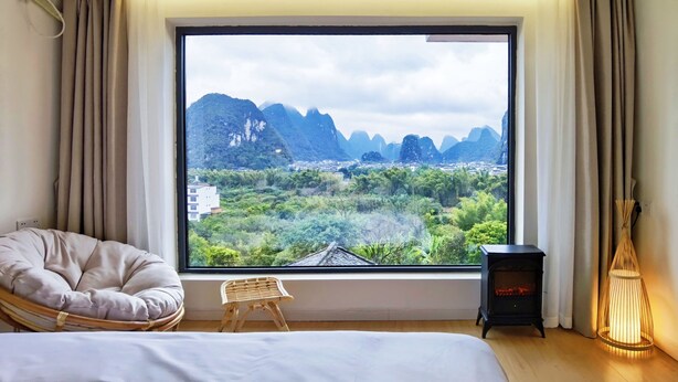 A bedroom with a large window offering a view of mountains and greenery. - Riverside Retreat Hotel (Guilin)