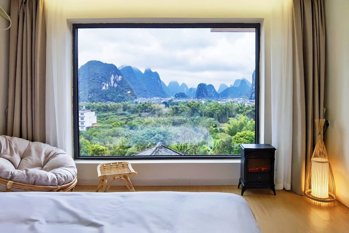 A bedroom with a large window offering a view of mountains and greenery.