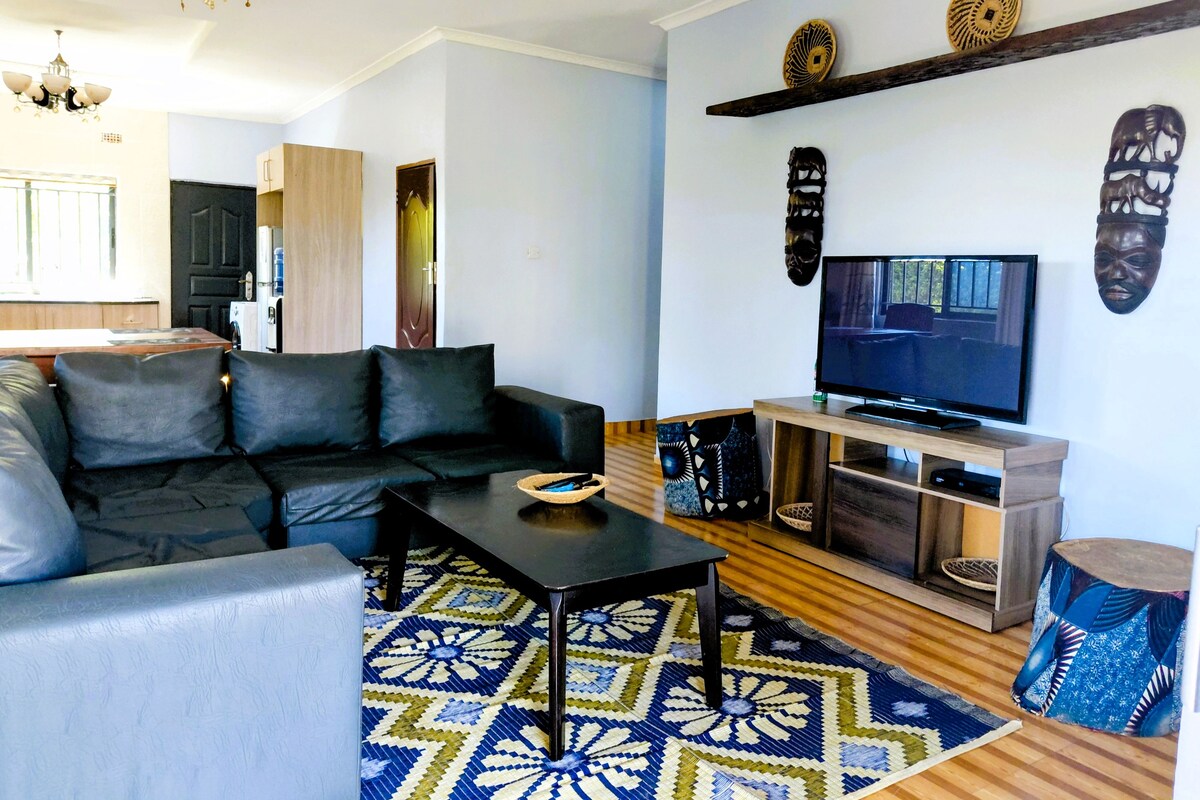 A living room with a black sofa, a coffee table, a television, and decorative masks on the wall.