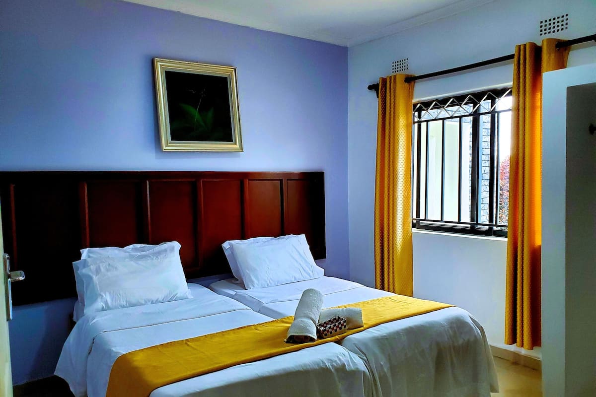 Habitació d'hotel amb dos llits, un panell de capçalera de fusta, un quadre a la paret i una finestra amb cortines.