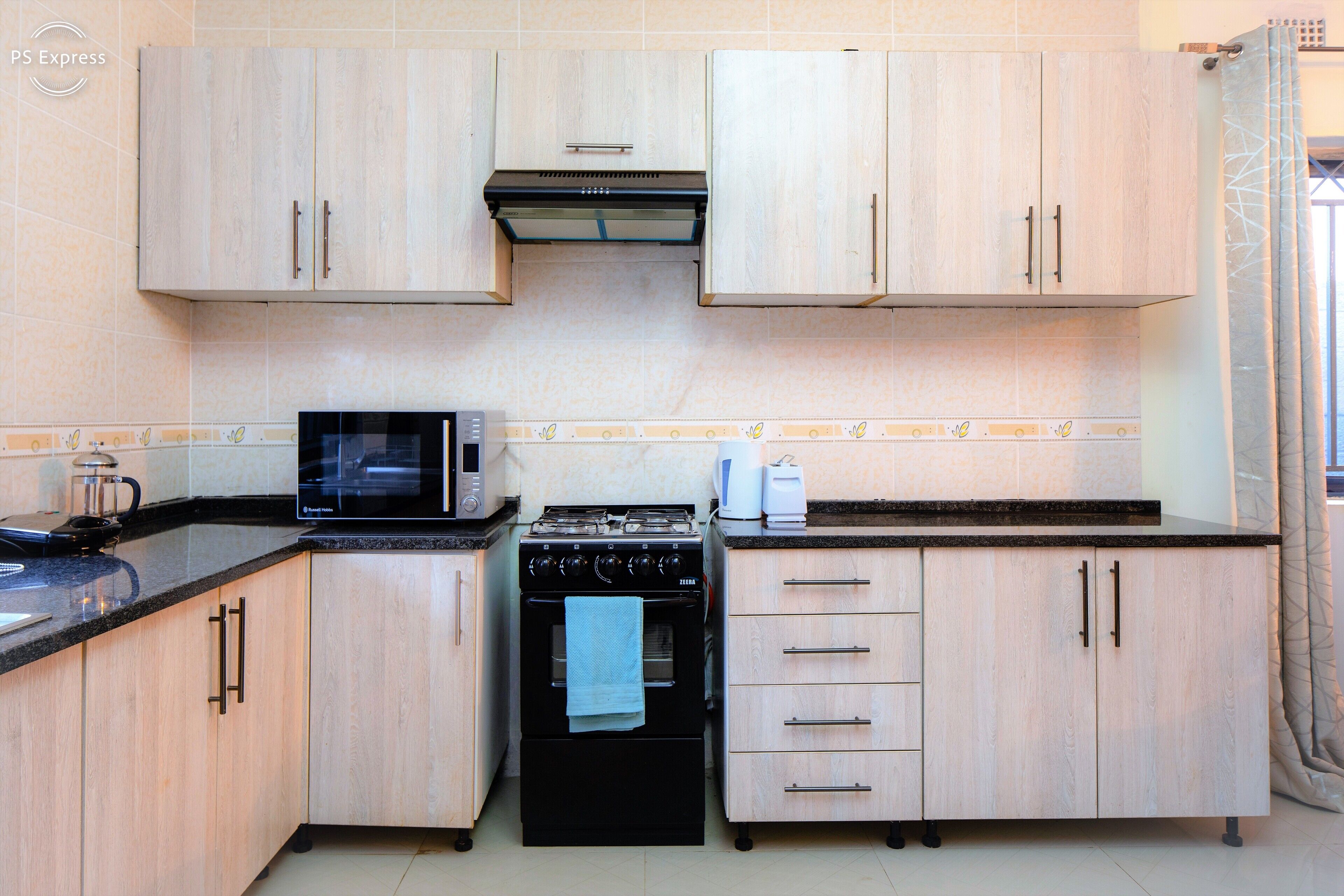 A compact kitchen with light wood cabinets, a black microwave, a stove, and a coffee maker.