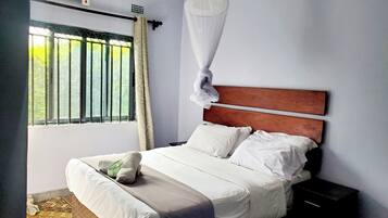 A neatly made bed with white linens, a wooden headboard, and a bedside table with a black nightstand.