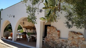 Un'area salotto esterna riparata con tavolo e sedie, pareti in pietra e un pergolato.