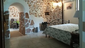 Una camera da letto con parete in pietra, un letto con copripiumino floreale, un comodino, una lampada e un piccolo tavolo con una sedia.