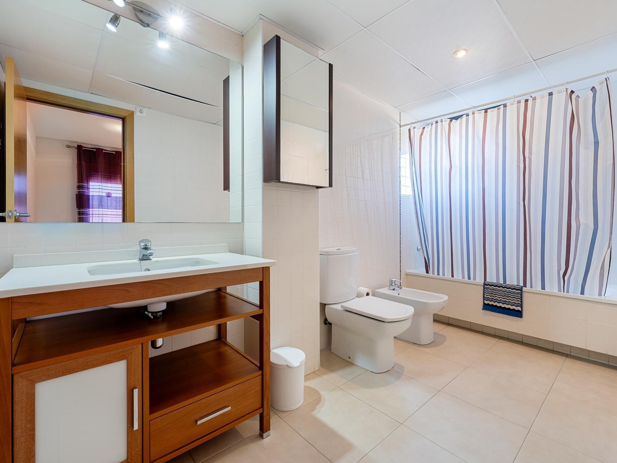 Un baño moderno con tocador de madera, un espejo grande, inodoro y bidé.