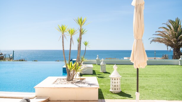 A pool area with a view of the sea, surrounded by palm trees and white lanterns. - Luxury Villa with infinity pool and breathtaking sea view (New Prices) (Urbanização Ponta da Gaivota, Lagos)