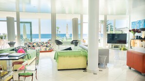 A spacious living area with a large window overlooking the sea, a sofa, a TV, and a dining table with chairs. - Luxury Villa with infinity pool and breathtaking sea view (New Prices) (Urbanização Ponta da Gaivota, Lagos)