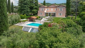 Una casa grande con piscina, rodeada de abundante vegetación y árboles altos.