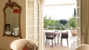 Una habitación interior con un espejo grande, una zona de comedor con sillas y una mesa, y un acceso abierto a un espacio exterior con plantas y vistas.