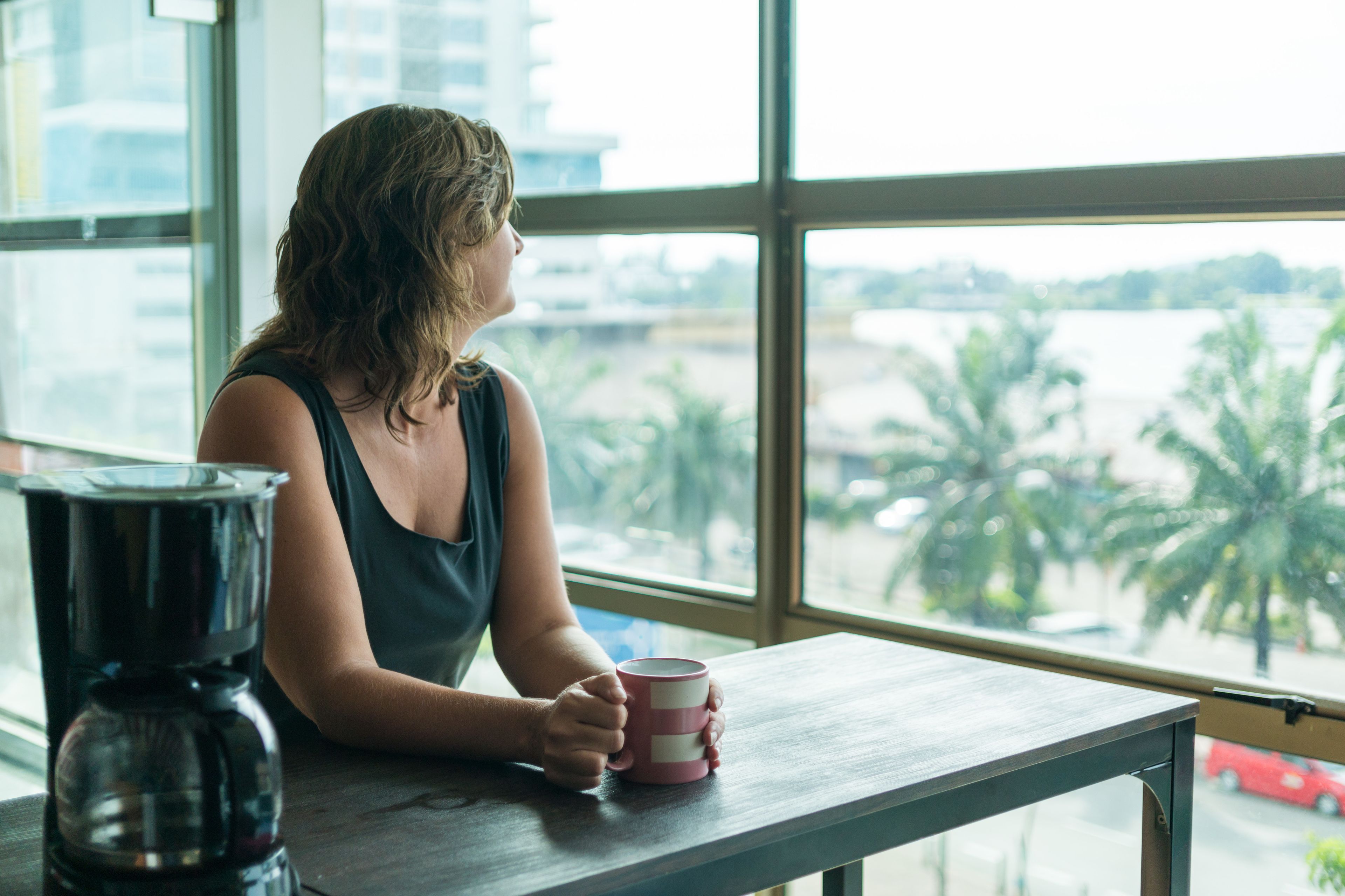 Una persona sentada a una mesa junto a una ventana con vistas a palmeras y una carretera.