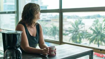 Una persona sentada a una mesa junto a una ventana con vistas a palmeras y una carretera.
