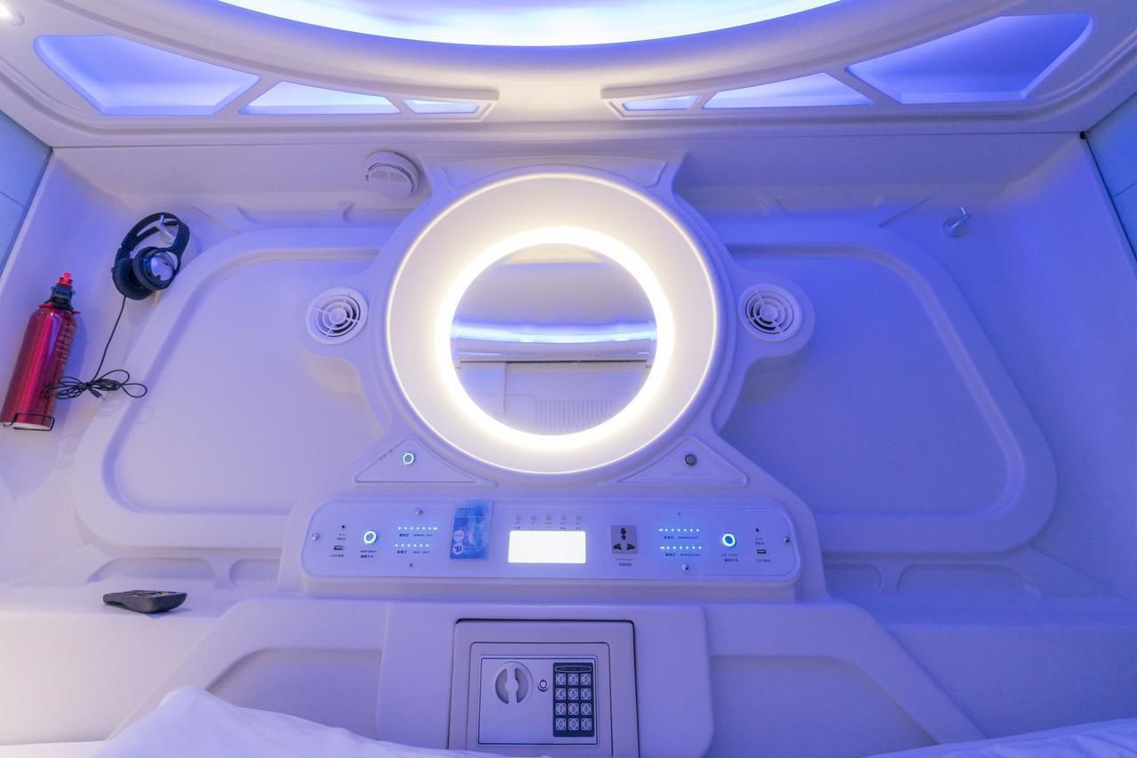 A modern, well-lit room with a circular mirror, control panel, and headphones on the wall.