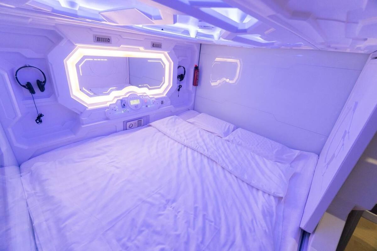 A modern, white-themed room with a bed, control panel, and headphones.