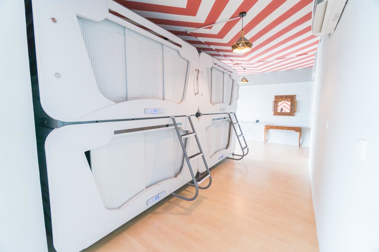 A modern, minimalist room with a white color scheme, featuring a bunk bed with a ladder, a wooden bench, and a striped ceiling.