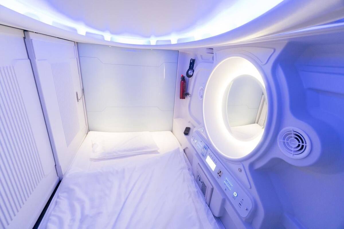 A modern, compact room with a bed, a control panel, and a circular window.