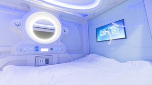 A modern, well-lit room with a bed, a control panel, and a digital display on the wall. - Seaview Capsule Hotel (Kota Kinabalu)