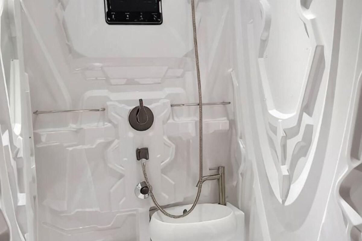 Un baño moderno con un lavamanos blanco, una ducha con cabezal de ducha manual y un inodoro.