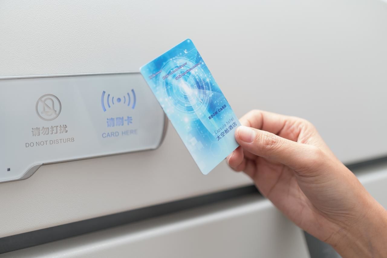 A hand holding a blue card with text and a logo, in front of a device with a "DO NOT DISTURB" sign and a "CARD HERE" label.