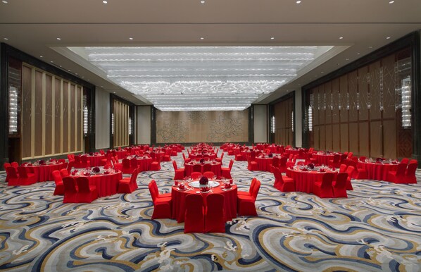 A large banquet hall with round tables and red chairs, arranged in rows, with a patterned carpet and a high ceiling with a light fixture. - Wanda Vista Shenyang (Shenyang)