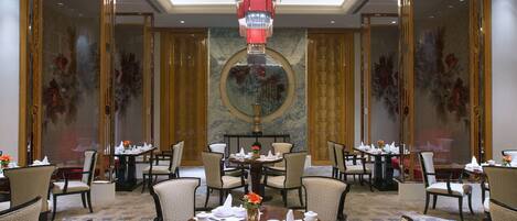 Un comedor formal con mesas redondas, sillas y una pieza decorativa en el centro.