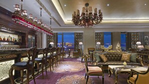 A luxurious hotel lobby with a bar area, seating arrangements, and a large chandelier.
