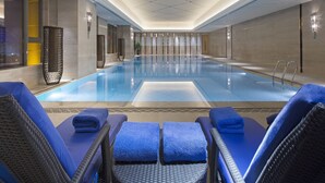 A large indoor swimming pool with lounge chairs and towels, surrounded by walls with decorative panels and lighting fixtures.