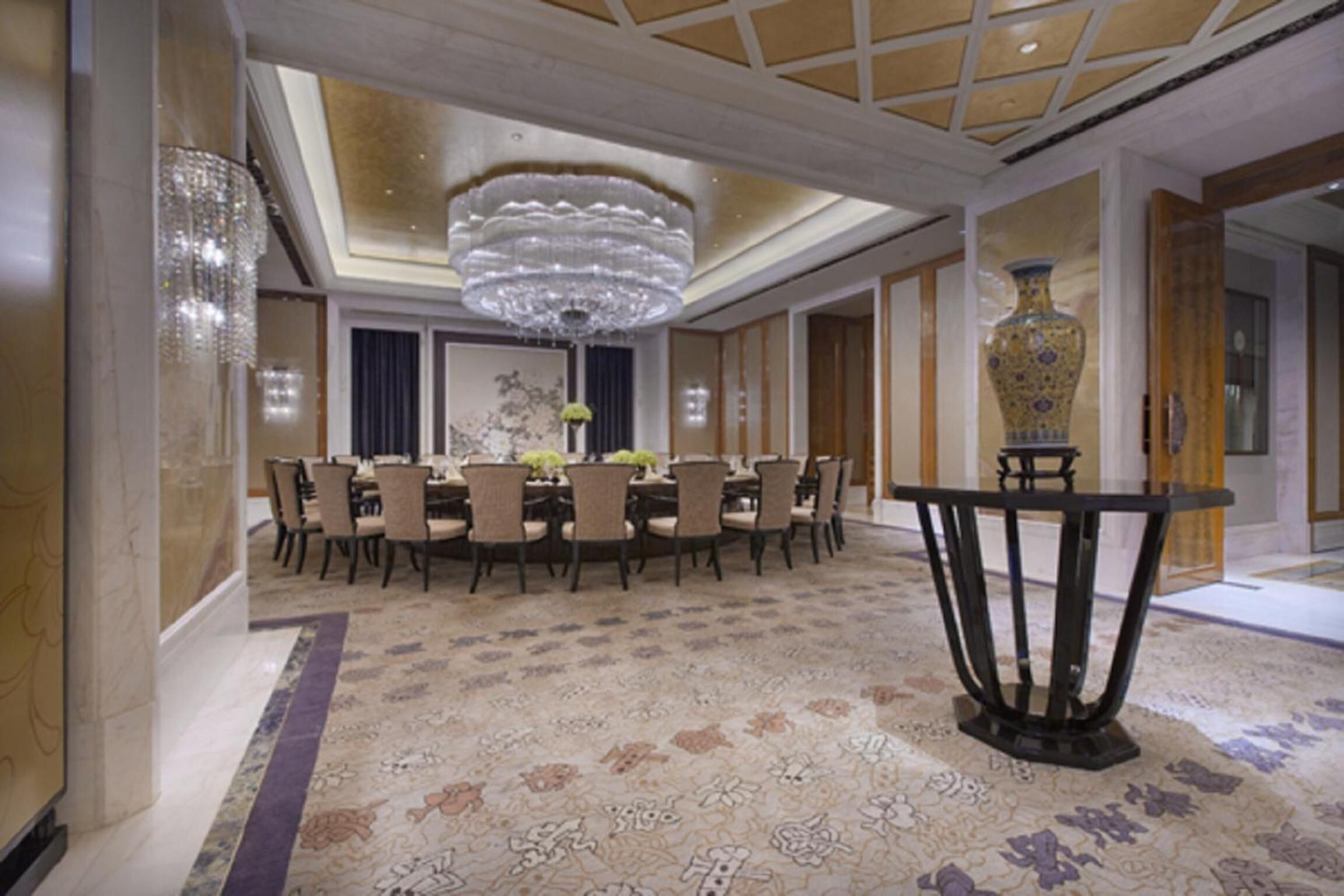 A formal dining area with a chandelier, a large vase, and a patterned carpet.