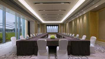 A conference room with a long table, white chairs, and a projector screen at the front.