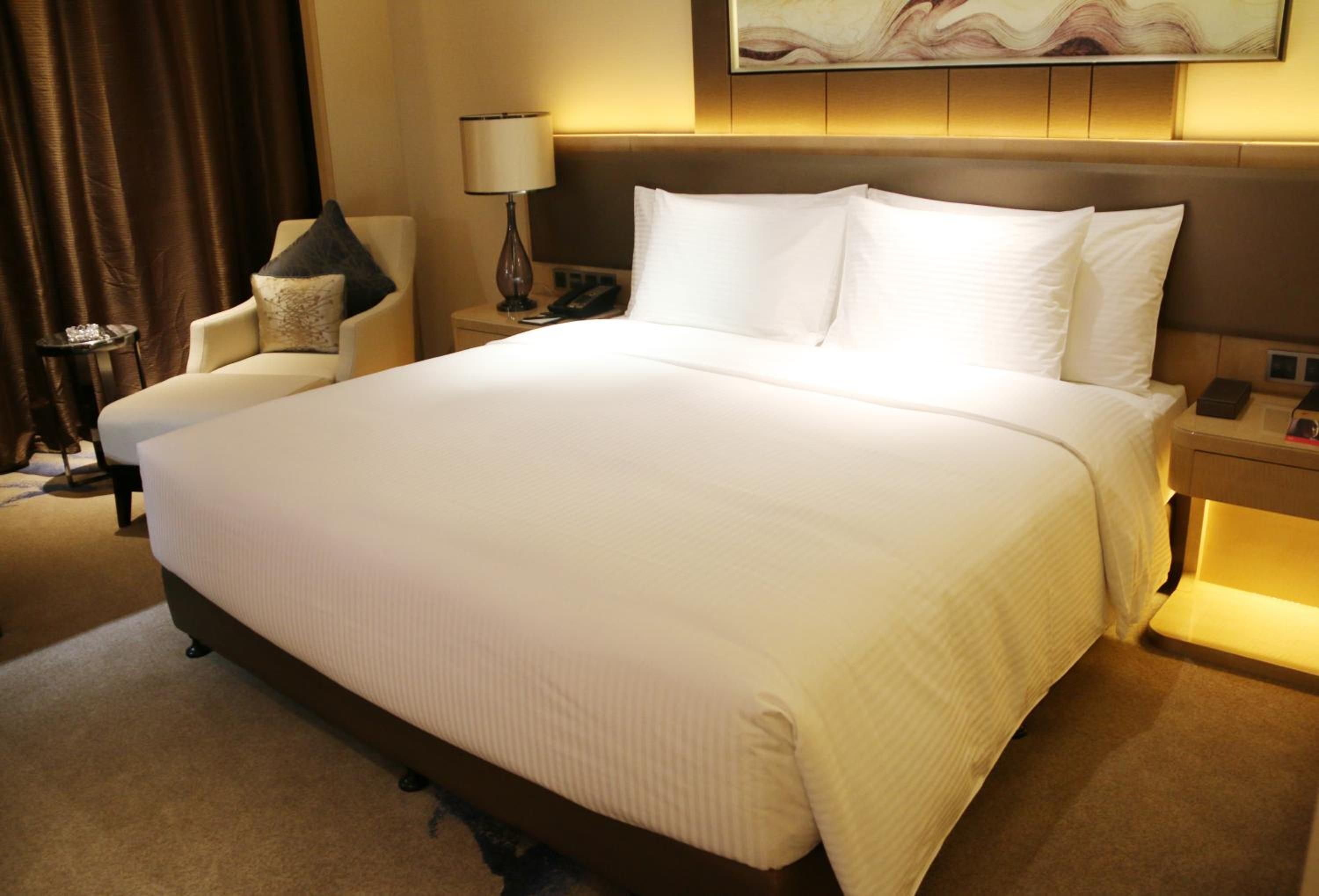 A hotel room with a large bed, a chair, a nightstand, and a lamp.