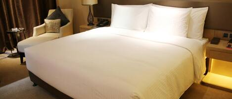 A hotel room with a large bed, a chair, a nightstand, and a lamp.