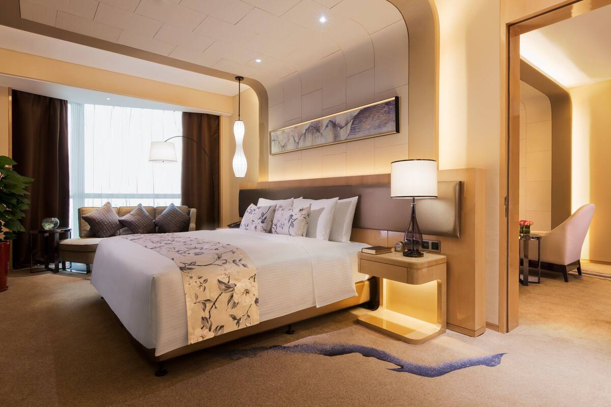 A modern hotel room with a large bed, bedside tables, a desk, and a chair.