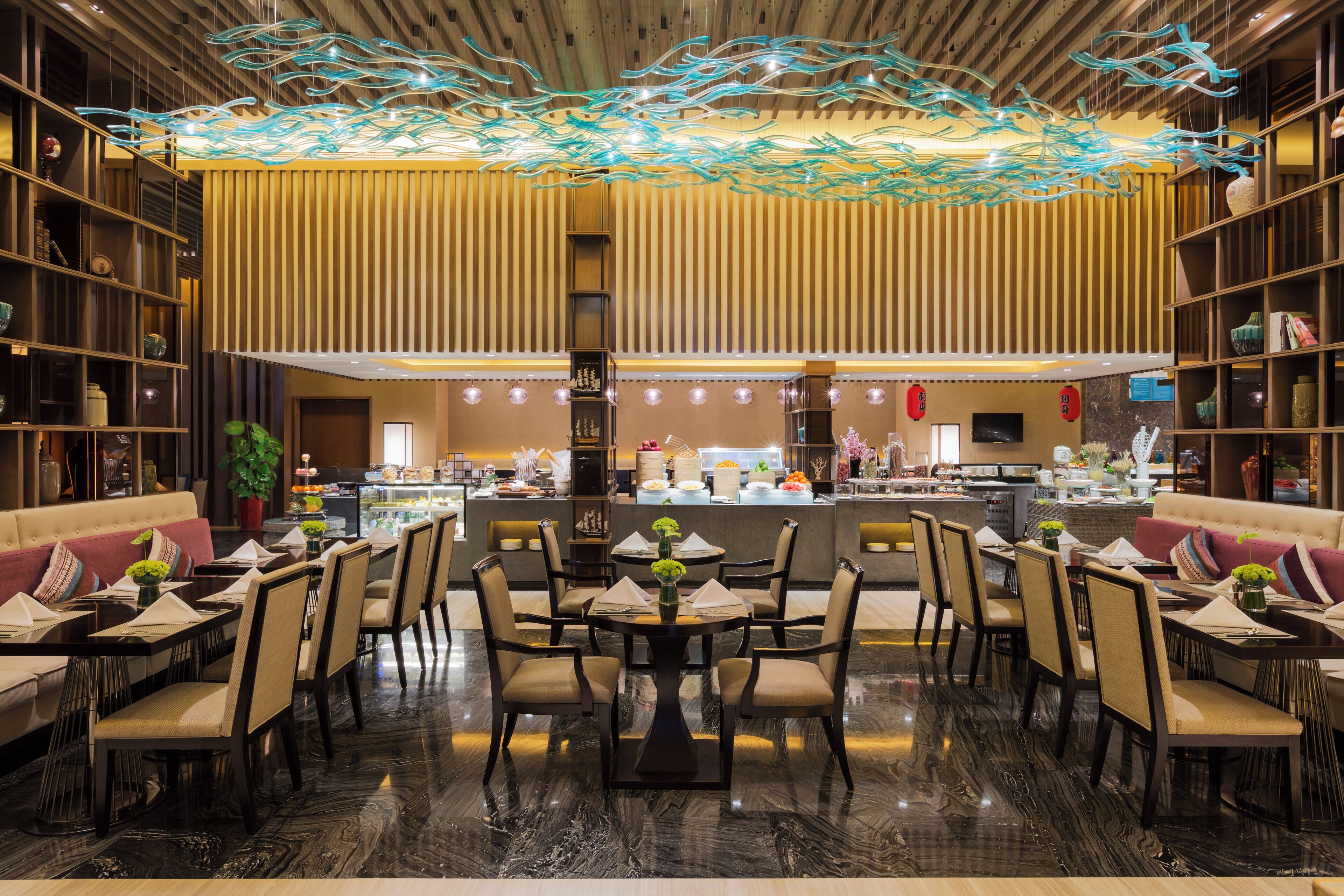 A modern restaurant with a central dining area, a bar, and a kitchen in the background.