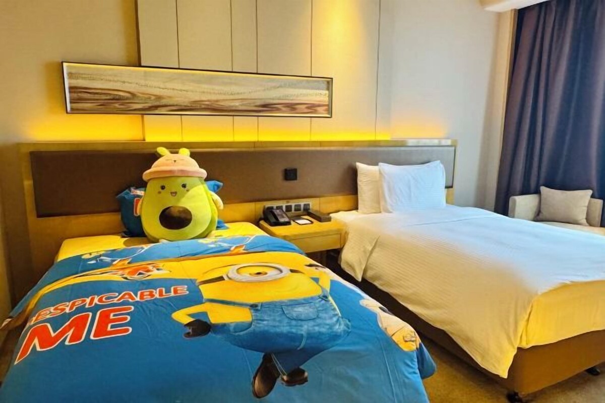 A hotel room with a bed, a nightstand, a lamp, and a large window with curtains.