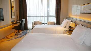 A hotel room with two beds, a desk, a chair, a TV, and a large window with curtains.