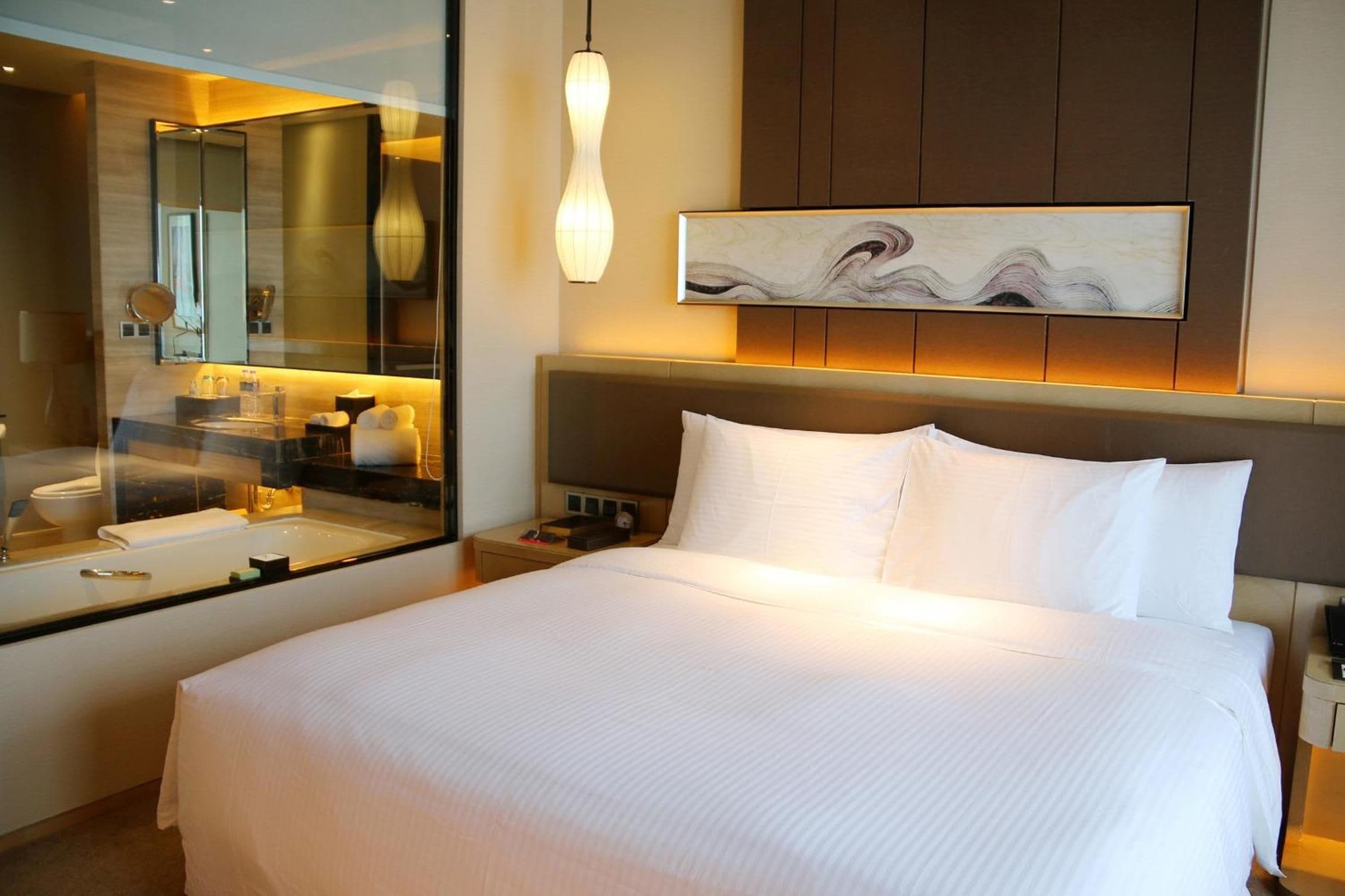 Una habitación de hotel con una cama grande, una mesita de noche, un espejo y una obra de arte en la pared.