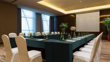 A conference room with a long table, white chairs, and a projector screen.