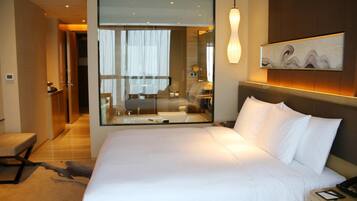Quarto de hotel moderno com uma cama grande, divisória de vidro, uma obra de arte na parede e mesa de cabeceira com telefone.