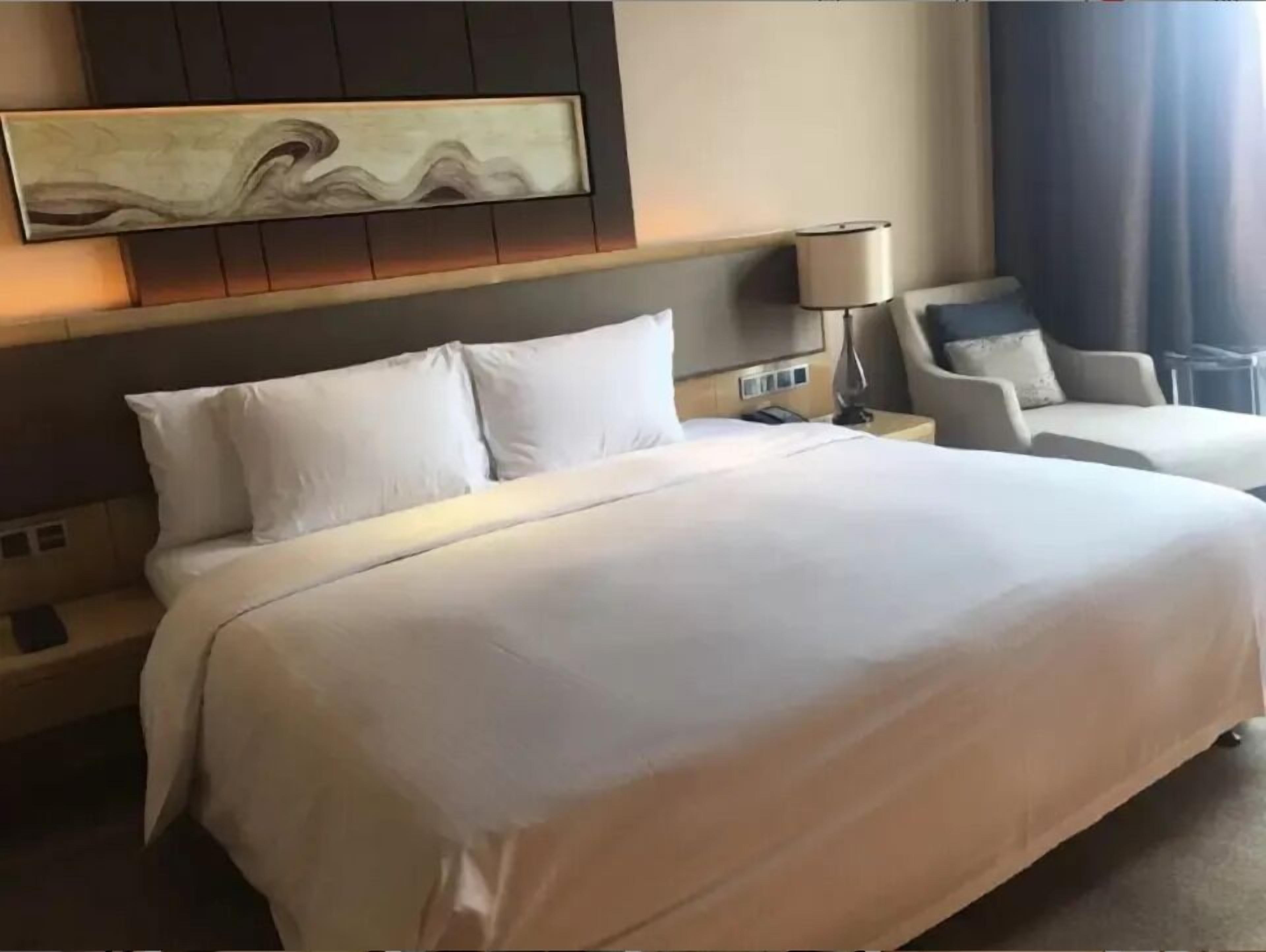 Una habitación de hotel con una cama grande, un cabecero con un panel decorativo, una mesita de noche con una lámpara y una silla.