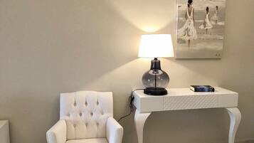 A white tufted armchair next to a white console table with a lamp and a book.