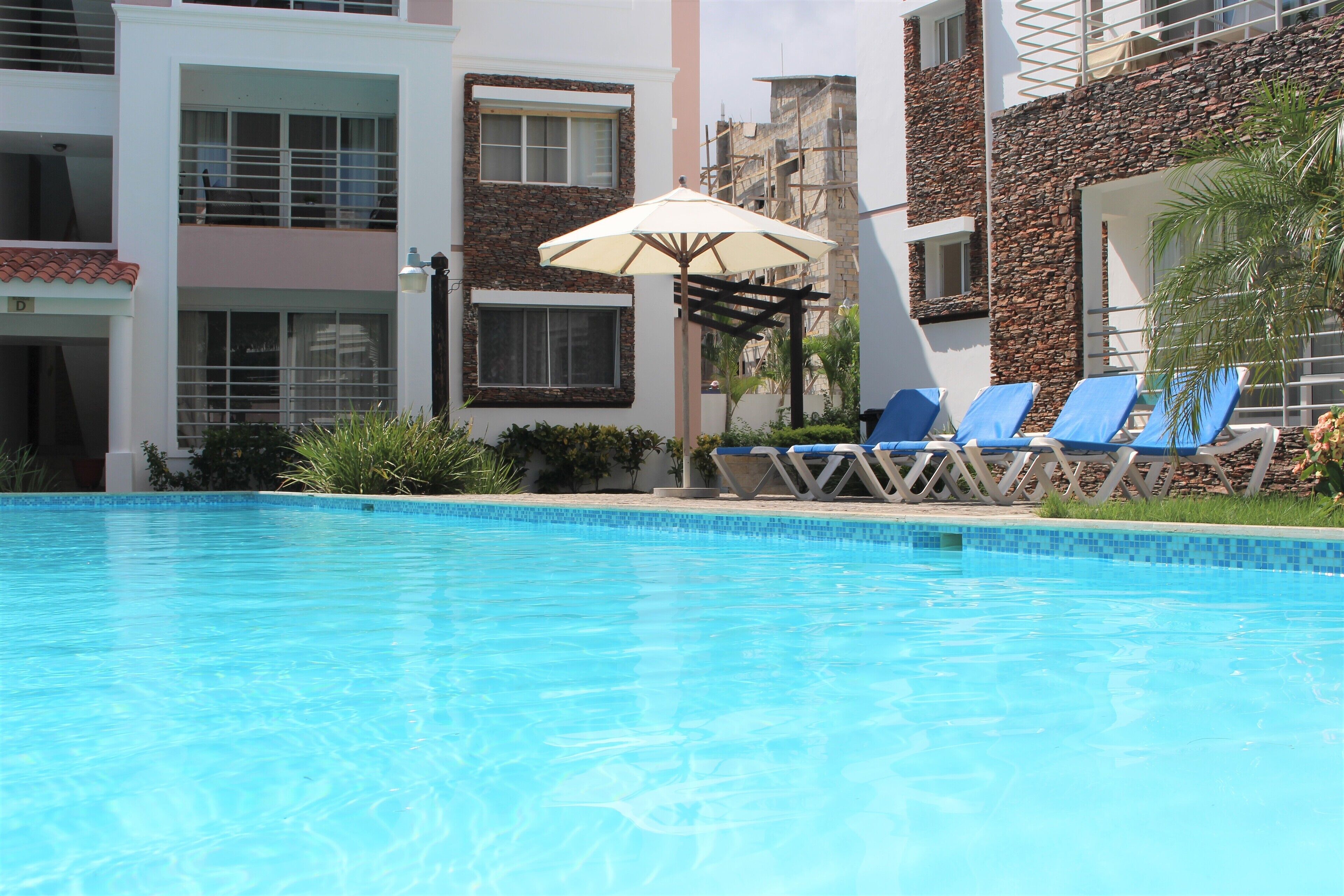 Une piscine à l’eau bleue, entourée de chaises longues et d’un parasol.