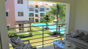 A balcony with wicker furniture, a pool, and a view of a multi-story building with balconies. - CORTE SEA Luxury apartment in the heart of Bavaro (Punta Cana)
