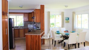 A modern kitchen with wooden cabinets, a built-in island, and a dining area with white chairs and a table set for four. - CORTE SEA Luxury apartment in the heart of Bavaro (Punta Cana)